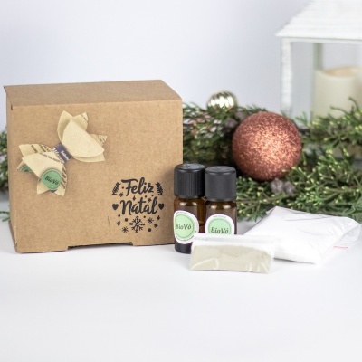 Conjunto para presente de Natal com caixa de cartão, garrafas de vidro, barro e tecidos junto de decoração natalícia.