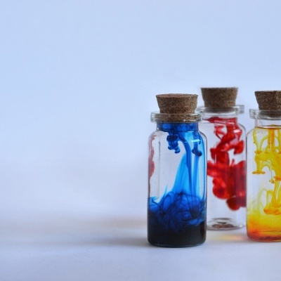 Três frascos de vidro com líquidos coloridos azul, vermelho e amarelo