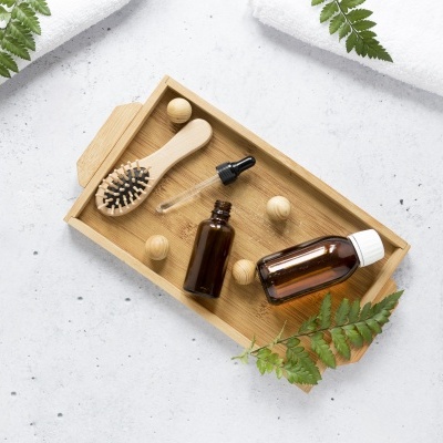 Bandeja de madeira com frascos âmbar, escova de cabelo, bolas de madeira e folhas verdes.
