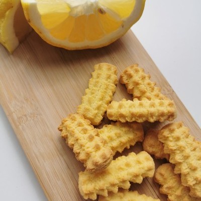 Biscoitos ondulados amarelos e fatias de limão num tabuleiro de madeira sobre fundo branco