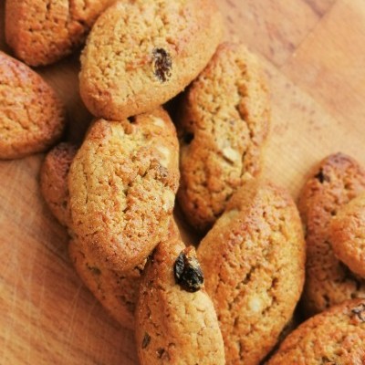 Biscoitos dourados com passas e frutos secos sobre madeira clara.