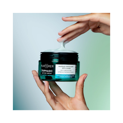 Frasco verde escuro de máscara capilar Fortifiant Anti-Casse com creme branco saindo e duas mãos a segurar