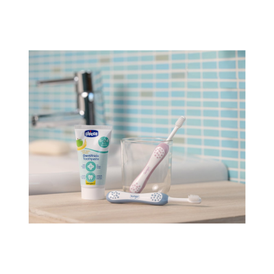 Pasta de dentes Chicco e duas escovas de dentes infantis em bancada com azulejos azuis ao fundo