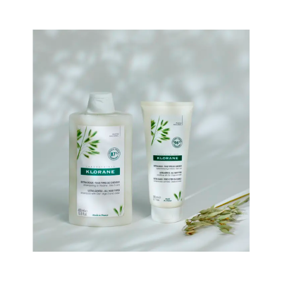 Dois produtos de cuidado capilar Klorane sobre superfície branca com planta seca ao lado