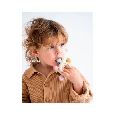 Criança a morder chocalho colorido em fundo branco.