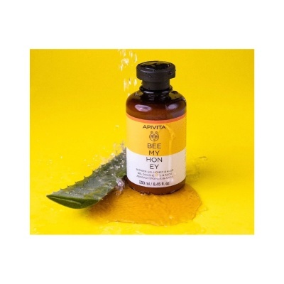 Frasco de gel de duche Apivita Bee My Honey junto a folha de aloe com líquido amarelo em fundo amarelo