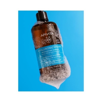 Frasco castanho de champô APIVITA com espuma sobre fundo azul