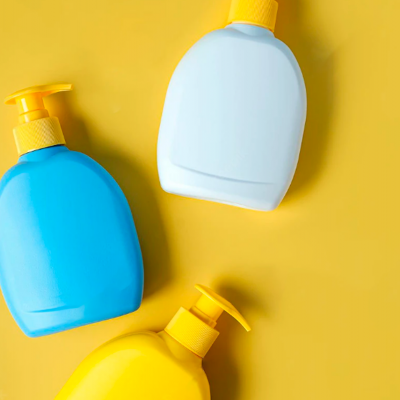 Três frascos plásticos coloridos com tampas de bomba sobre fundo amarelo.