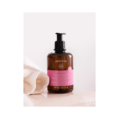 Frasco de gel de limpeza íntima Apivita com doseador preto e etiqueta rosa ao lado de uma toalha branca.