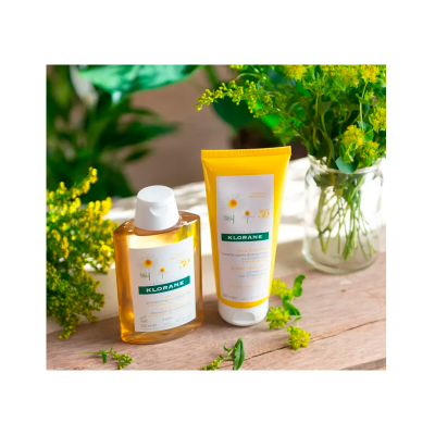 Produtos Klorane em frasco e tubo amarelos com flores amarelas ao redor sobre mesa de madeira