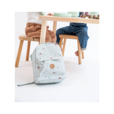 Mochila infantil azul clara com padrão de animais e bolso frontal junto a mesa e cadeiras de madeira.