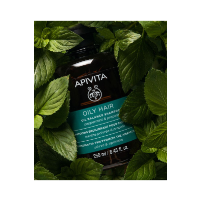 Frasco de champô APIVITA OILY HAIR rodeado por folhas verdes