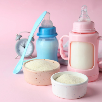 Biberões com leite, recipientes de pó de bebé, colher e despertador sobre fundo rosa