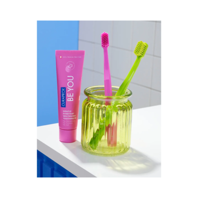 Tubo de pasta dentífrica cor-de-rosa e duas escovas de dentes rosa e verde em frasco de vidro verde