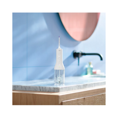 Irrigador oral branco sobre bancada de mármore com parede azul e torneira preta no fundo