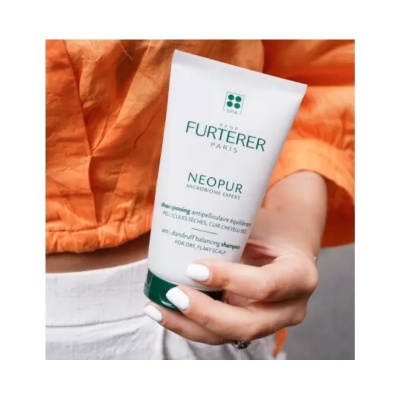 Frasco de champô Rene Furterer Neopur com tampa verde segurado por mão com unhas brancas e pessoa com camisa laranja.