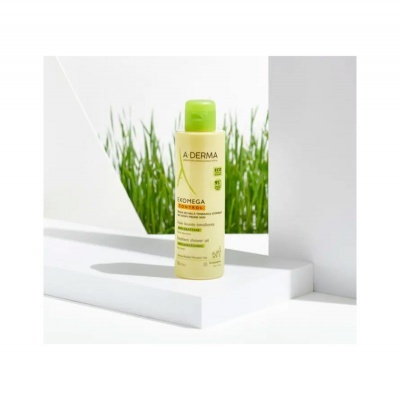 Frasco amarelo com tampa verde de A-Derma Exomega em superfície branca com relva ao fundo