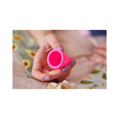 Mão a segurar copo menstrual rosa em fundo com tecidos estampados