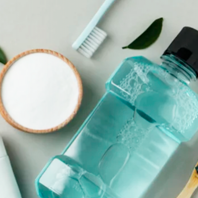 Frasco azul de elixir bucal, escovas de dentes, recipiente de madeira com pó branco e folhas verdes