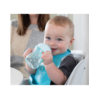 Bebé a beber de copo azul na cadeira alta, usando babete azul.