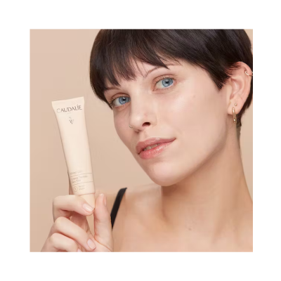 Mulher a segurar tubo bege claro de creme facial CAUDALIE com texto impresso