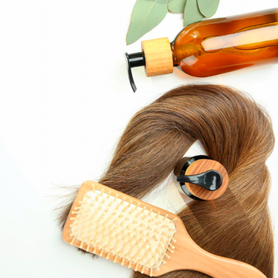 frasco âmbar com tampa de madeira, escova de cabelo de madeira com cerdas brancas e cabelo castanho enrolado