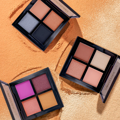 Três paletas de sombra de olhos com diversas cores sobre fundo texturizado cor de salmão