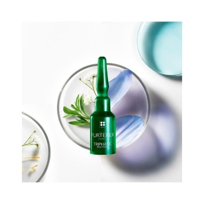 Frasco verde Furterer Triphasic sobre pratos com flores e pétalas