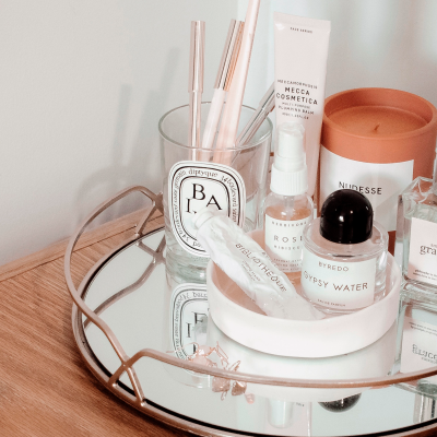 Produtos de cosmética e fragrâncias numa bandeja espelhada com moldura dourada sobre superfície de madeira