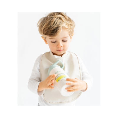 Criança com babete bege segurando copo branco com desenho de carro amarelo