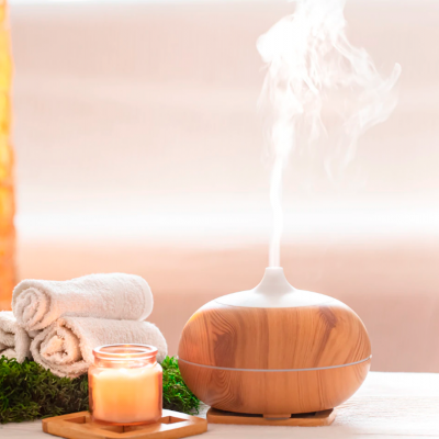 Difusor de aroma de madeira clara com vapor, junto a toalhas brancas, musgo e vela laranja