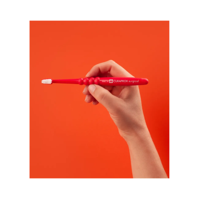 Escova de dentes vermelha com texto CURAPROX surgical em fundo laranja