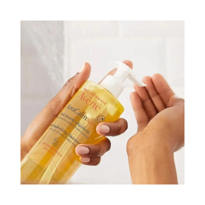 Frasco amarelo de gel de banho Avène com doseador, mãos a usar o produto.