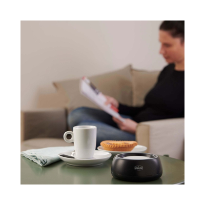 Mesa com chávena branca, tarte, recipiente preto Chicco e pessoa em sofá