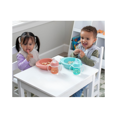 Duas crianças a comer em mesa branca com pratos rosa e azul e copos de treino laranja e azul