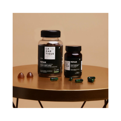 Frascos de suplementos LAZARTIGUE REPAIR com gomas e cápsulas numa mesa dourada