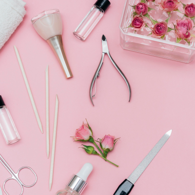 Ferramentas e produtos para manicure sobre fundo rosa com flores rosas em recipiente transparente.