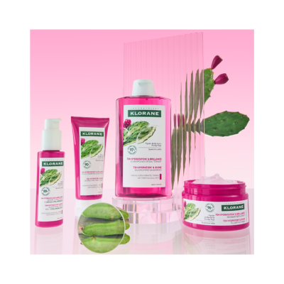 Produtos Klorane com rótulos verdes e brancos em frascos rosa e fundo com planta figueira da índia