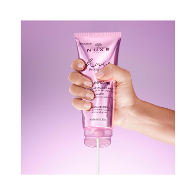 Frasco de champô NUXE cor-de-rosa metálico com líquido a sair