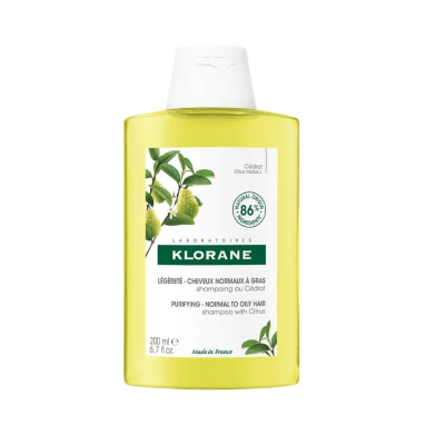 Frasco amarelo de champô Klorane com tampa branca e rótulo com texto e imagem de frutas cítricas.