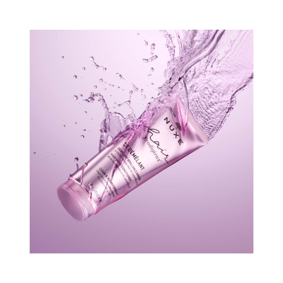 Tubo rosa de creme para cabelo NUxE a meio submerso em água com fundo lilás.