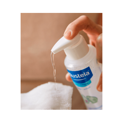 Frasco de doseador Mustela a dispensar líquido sobre toalha branca.