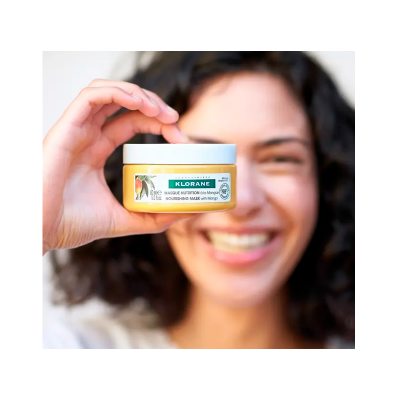 Frasco de máscara nutritiva Klorane amarelo sendo segurado por mulher sorridente.