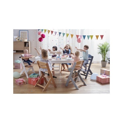 Crianças em torno de mesa branca redonda com cadeiras de madeira, decoração de festa com balões e presentes