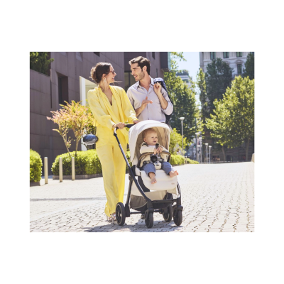 Bebé num carrinho bege com estrutura preta, mulher em fato amarelo e homem em camisa azul num passeio urbano