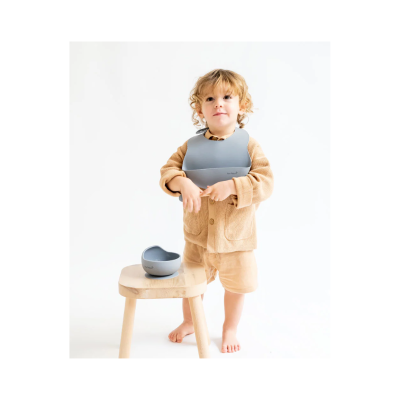Criança com babete cinzento e tigela em banco de madeira