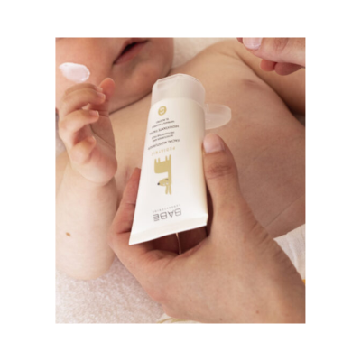 Creme para bebé num tubo branco com tampa transparente, segurado por uma mão junto ao braço e rosto de um bebé.