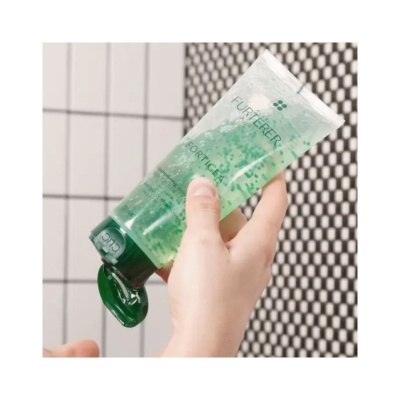 Bisnaga de gel verde transparente com tampa verde, segurada por mãos em fundo de azulejos