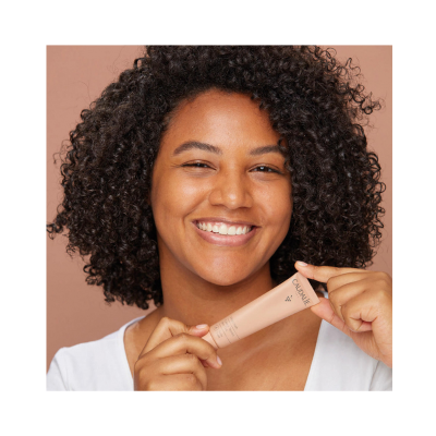 Mulher sorridente a segurar tubo de produto Caudalie cor bege