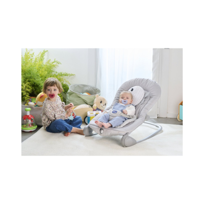 Cadeira de bebé cinzenta com almofada de peixe e bebé sentado, menina com chupeta sentada no tapete com brinquedos ao fundo